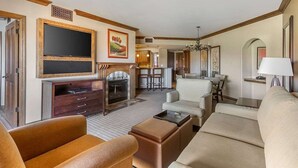 A hotel living room with a fireplace, a television, and a dining area.