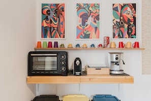 A kitchenette with a microwave, coffee maker, and toaster. Above the counter, there are colorful cups and three artworks.