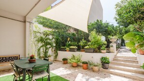 A patio with a table and chairs, surrounded by potted plants and a staircase leading to a covered area.