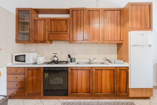 Una cocina con armarios de madera, microondas, estufa, horno y refrigerador.
