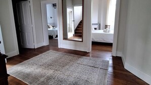 Ein geräumiger Raum mit Holzboden, einem großen, gemusterten Teppich und einem Spiegel mit Holzrahmen.