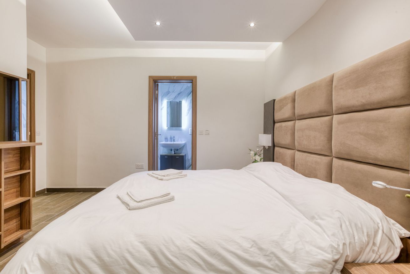 A modern hotel room with a large bed, a wooden wardrobe, and a bathroom visible through a door.