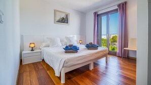 Una camera da letto con un letto, comodini, una finestra con tende e vista sul verde circostante.