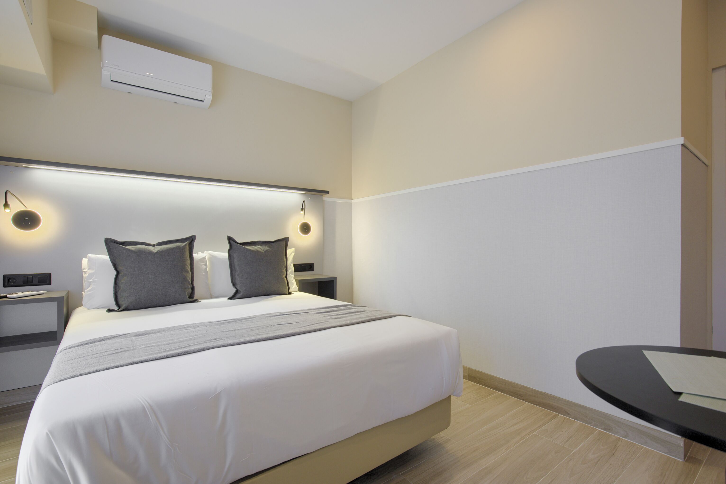 Una habitación de hotel moderna con una cama grande, mesitas de noche, un escritorio y un equipo de aire acondicionado.