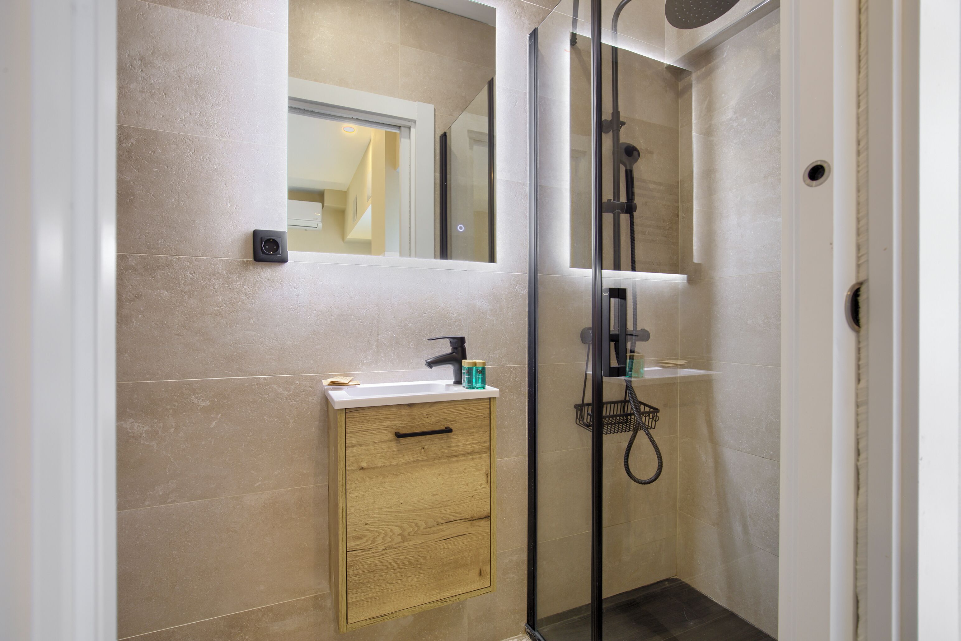 Un baño moderno con ducha envuelta en vidrio, un mueble de madera con lavamanos y un espejo sobre el mueble.