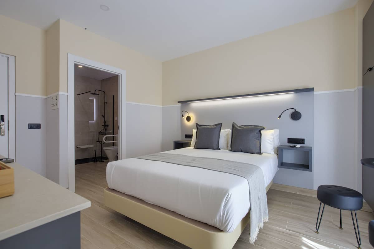 Quarto moderno com uma cama grande, mesas de cabeceira e um banheiro visível por uma porta aberta.