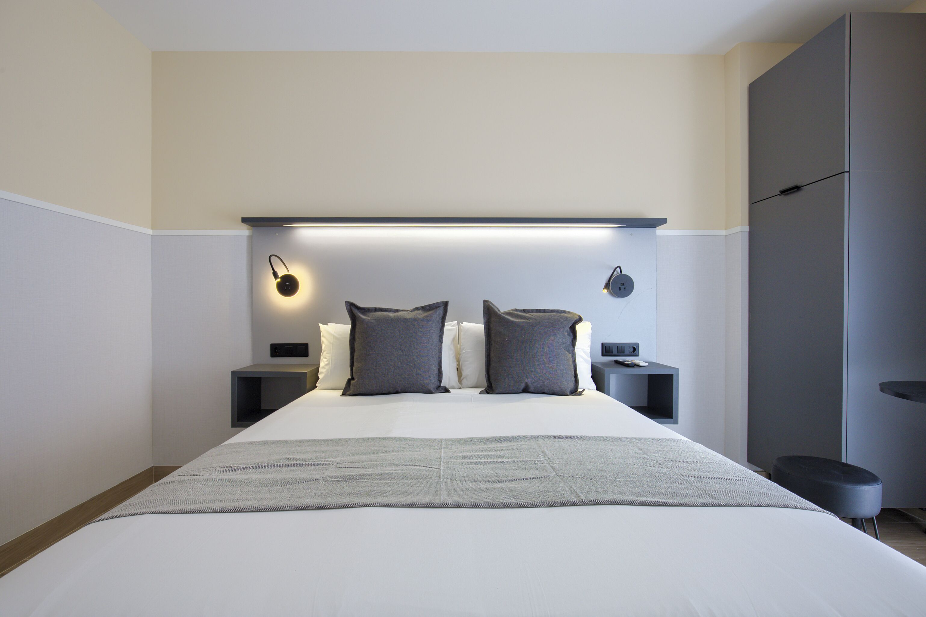 A modern hotel room with a large bed, bedside tables, and a wardrobe.