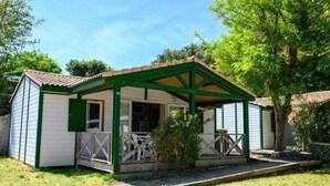 Un petit bâtiment d’un seul étage, à l’extérieur vert et blanc, avec un toit en tuiles et une véranda couverte dotée de chaises blanches.