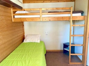 Quarto com beliche, colcha verde, escada de madeira e pequena prateleira.