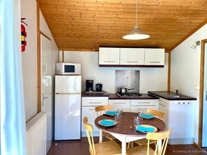 Cozinha compacta com eletrodomésticos brancos, uma mesa redonda com cadeiras e teto de madeira.