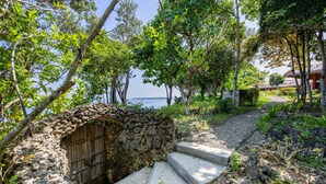 A stone structure with a wooden door, surrounded by lush greenery and a clear view of the sea. - CLIFF HOUSE at LILI CLIFF (Ferrol)