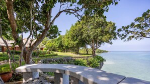 A stone bench overlooking a calm sea, surrounded by lush greenery and trees. - CLIFF HOUSE at LILI CLIFF (Ferrol)