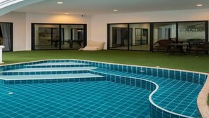 Ein modernes, überdachtes Schwimmbecken mit bogenförmigem Design, umgeben von einer überdachten Terrasse mit Sitzgelegenheiten.