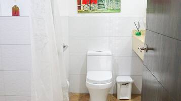Un baño con inodoro, un cubo de basura, cortina de ducha e imagen de una bicicleta en la pared.
