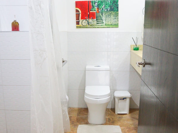 A bathroom with a toilet, a trash bin, a shower curtain, and a picture of a bicycle on the wall. - HOTEL HYM SAS (Palmira)