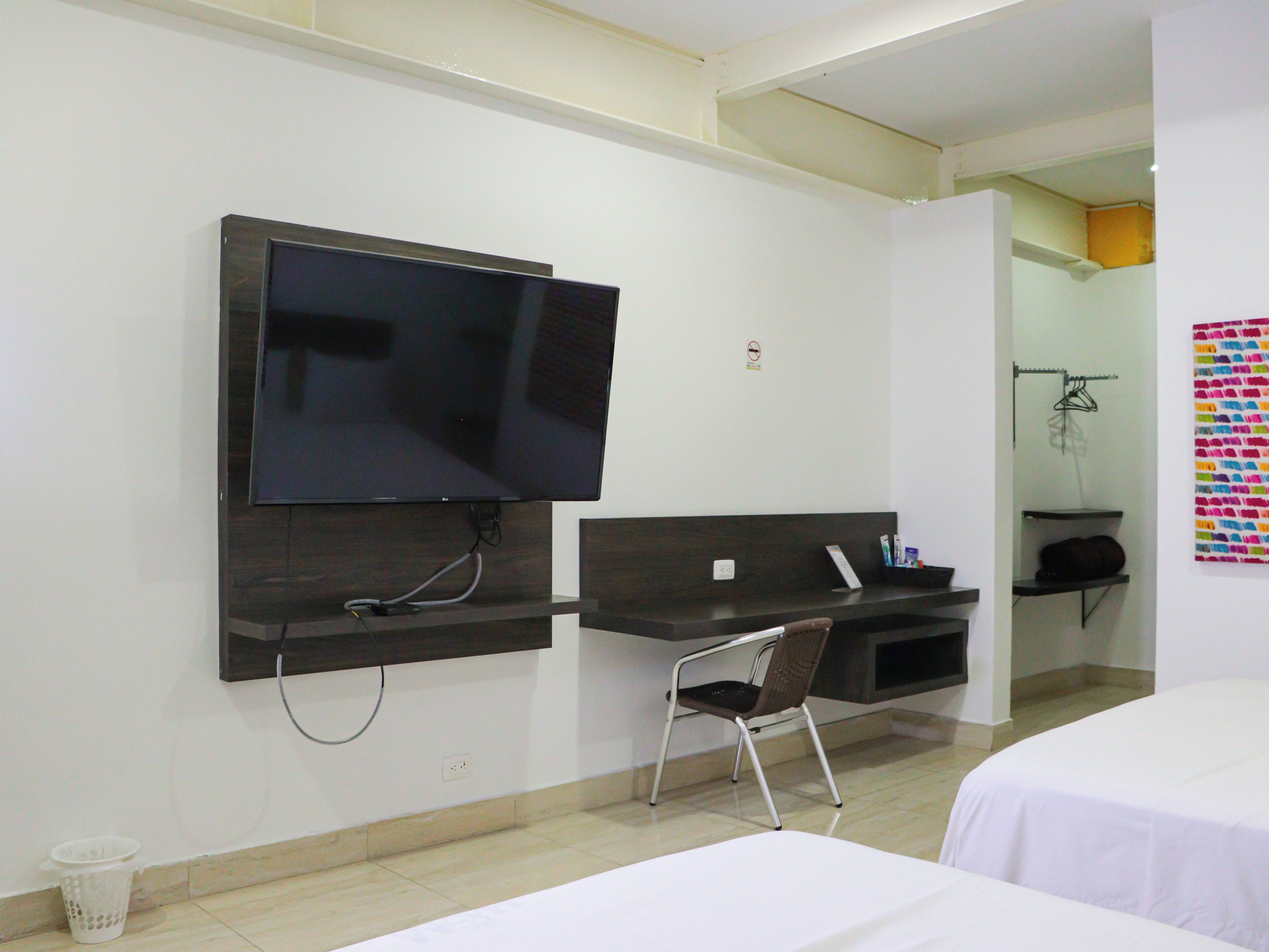 A hotel room with a flat-screen TV mounted on the wall, a desk with a chair, and a bed.