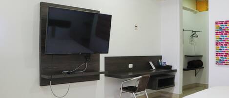 A hotel room with a flat-screen TV mounted on the wall, a desk with a chair, and a bed.