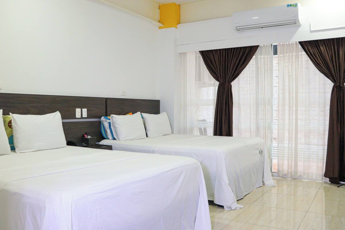 Une chambre d’hôtel avec deux lits, une table de chevet, un appareil de climatisation et une fenêtre avec des rideaux.