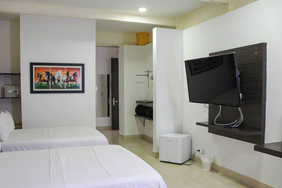 Une chambre d’hôtel avec deux lits, une télévision, une petite armoire blanche et une salle de bain visible à travers une porte ouverte.