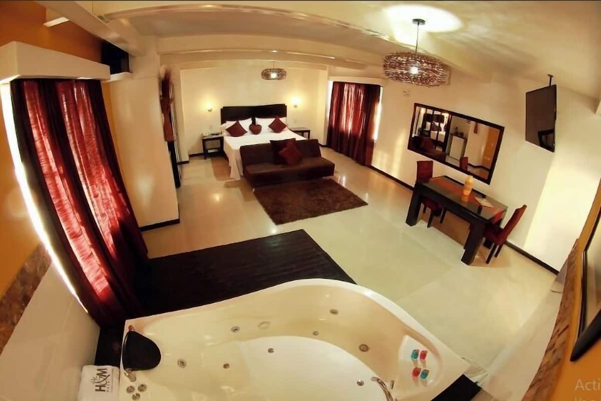 Une chambre d’hôtel moderne dotée d’un grand lit, d’un coin salon avec un canapé, d’une table à manger et d’une grande baignoire.