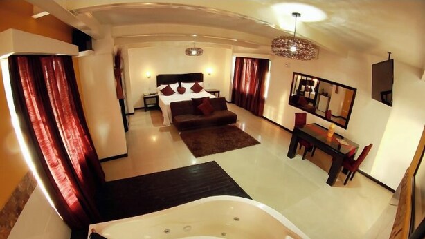 A modern hotel room with a large bed, a sitting area with a sofa, a dining table, and a large bathtub. - HOTEL HYM SAS (Palmira)