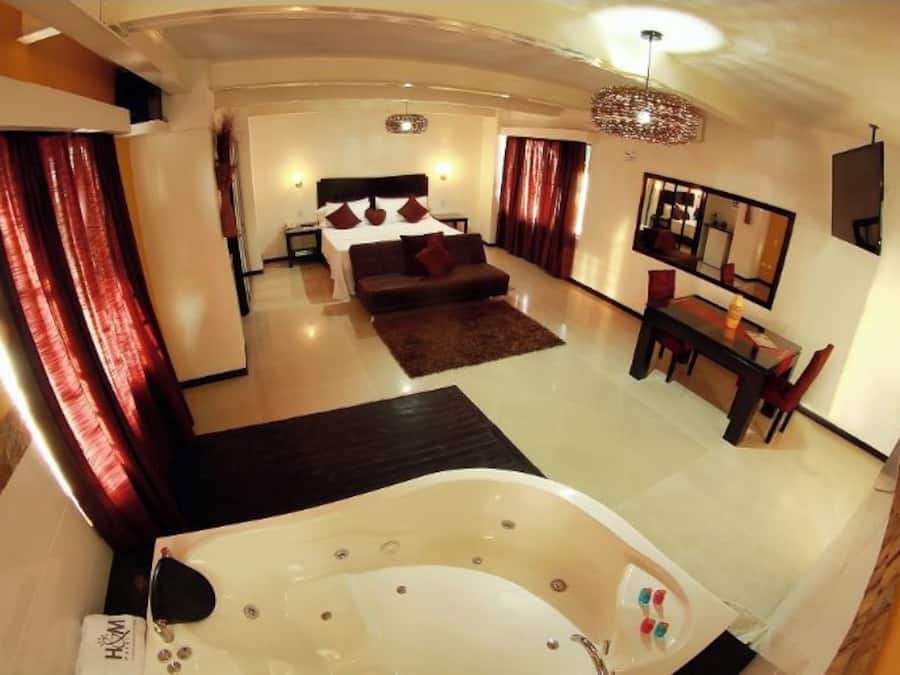 Una habitación de hotel moderna con una cama grande, un área de descanso con sofá, una mesa de comedor y una bañera espaciosa.