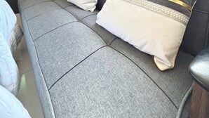 A modern hotel room with a grey sofa, two pillows, a small table with a lamp, and a window with curtains. - Spacious Studio @Horizon 101 with Aesthetics View (Cebu City)