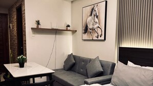 A modern hotel room with a bed, a grey sofa, a small table with a plant, and a painting of a horse on the wall. - Spacious Studio @Horizon 101 with Aesthetics View (Cebu City)