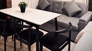 A modern living room with a grey sofa, a white coffee table, and black chairs. There is a painting of a horse on the wall and a small shelf with plants. - Spacious Studio @Horizon 101 with Aesthetics View (Cebu City)