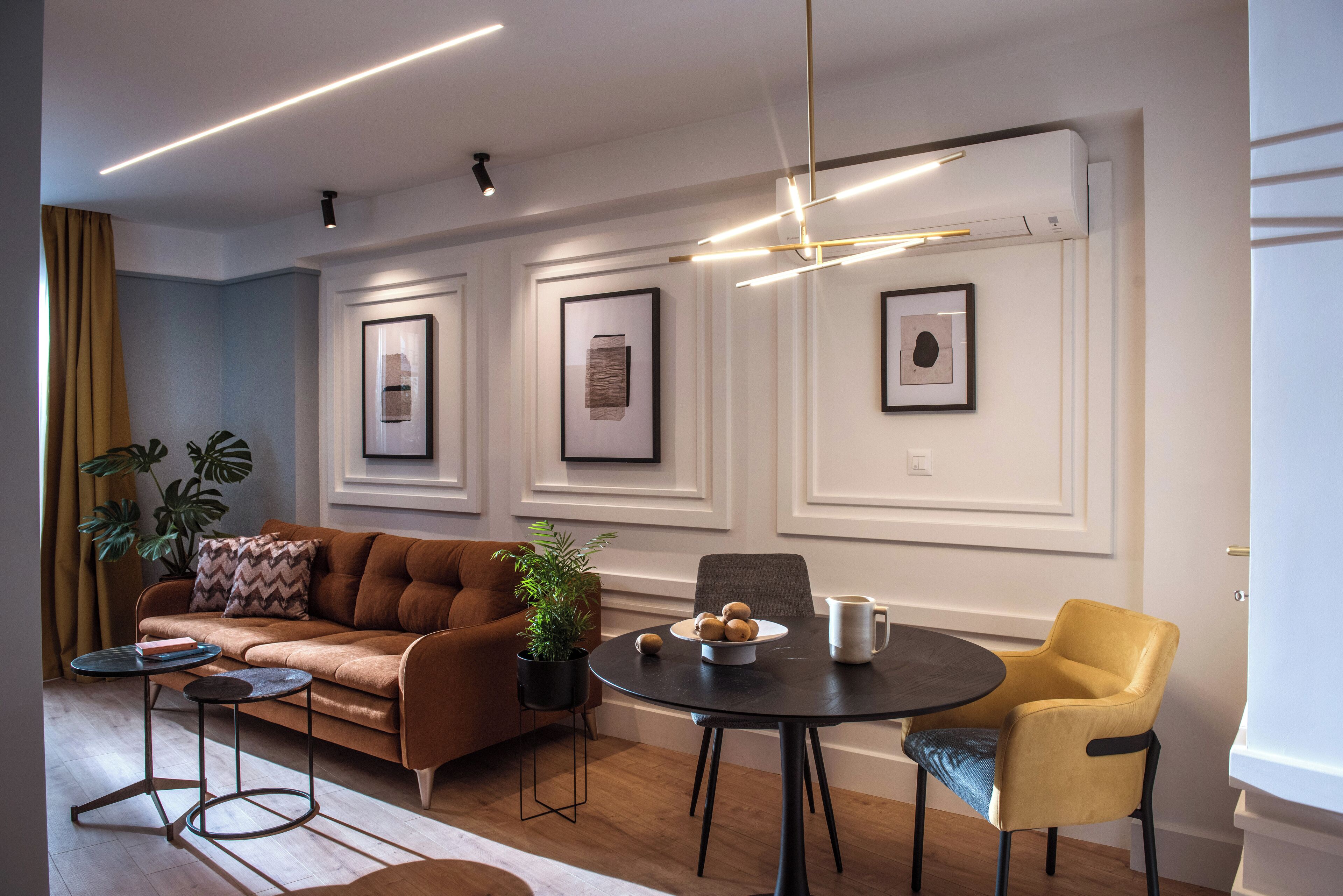 A modern living room with a brown sofa, a yellow chair, a round table, and framed artwork on the walls.