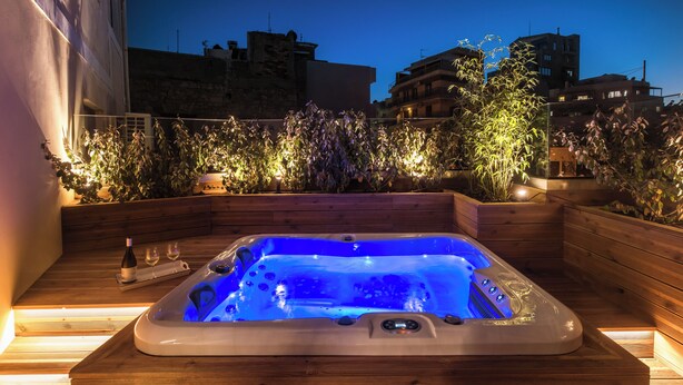 Un jacuzzi con muelle de madera y vista a edificios y plantas al anochecer.