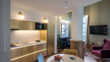 Una cocina moderna con electrodomésticos integrados, un comedor con una mesa redonda y sillas, y una sala de estar con sofá y televisor.