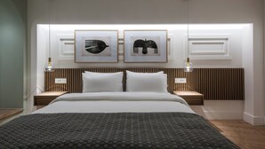 Una habitación de hotel moderna con una cama grande, dos mesitas de noche y dos lámparas fijadas a la pared.