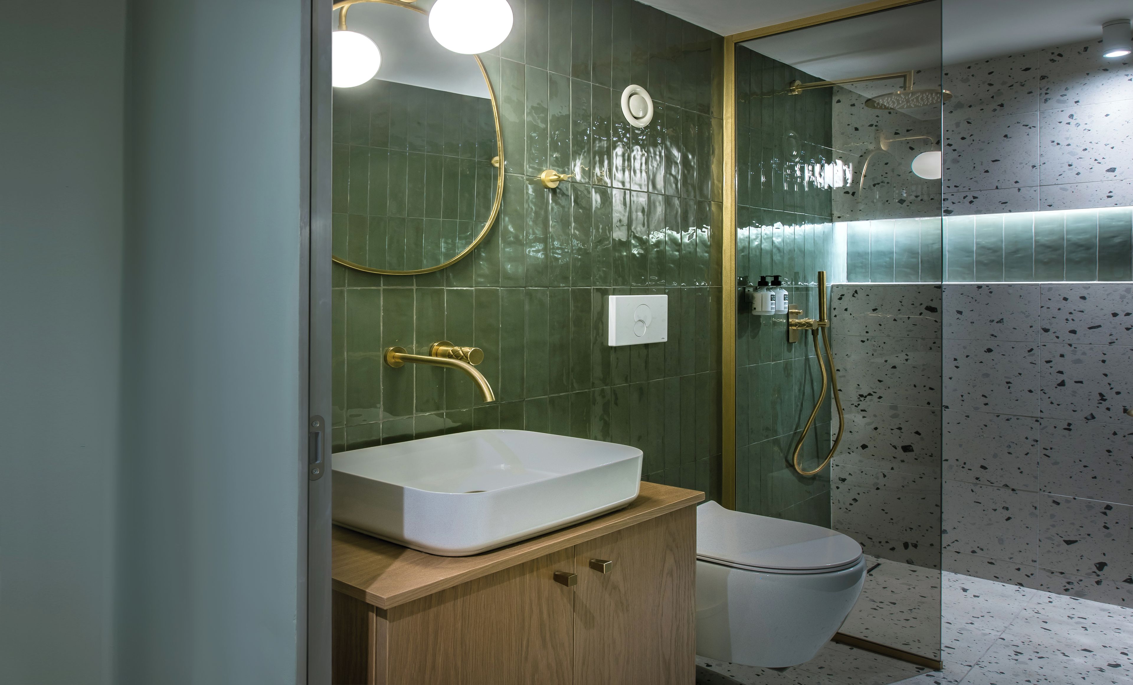 Een moderne badkamer met uitzicht op zee, met een groot wit wastafel, een gouden kraan en een douchecabine met glazen wanden.