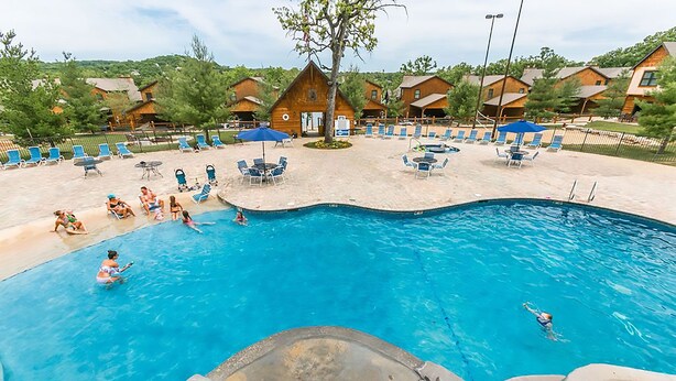 Una piscina con sillas de descanso y sombrillas, rodeada de cabañas de madera.