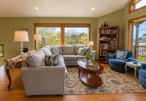 A living room with a sectional sofa, a coffee table, a bookshelf, and a view of the outdoors.