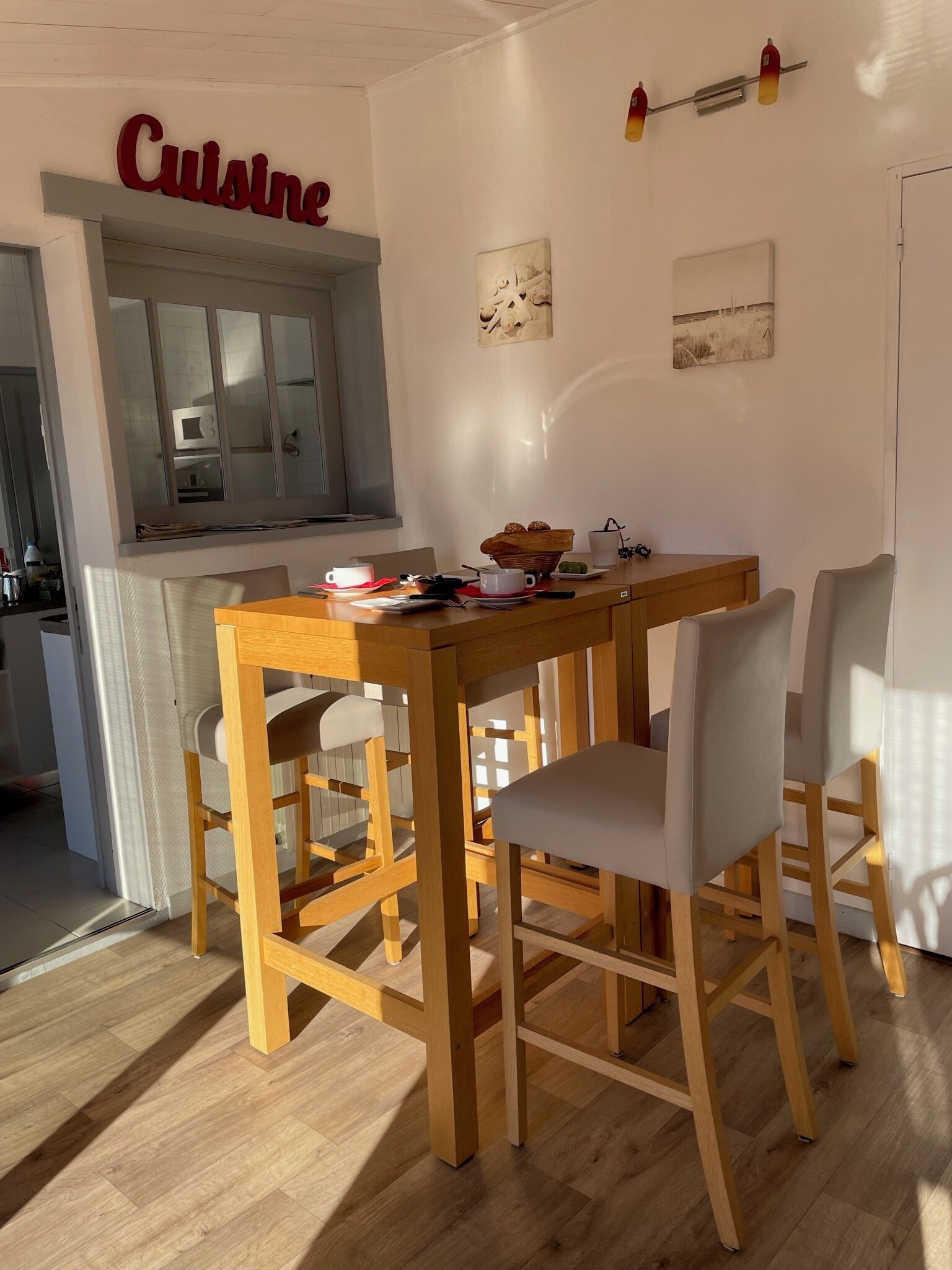 A dining area with a wooden table and chairs, a kitchen area with a microwave, and artwork on the walls.