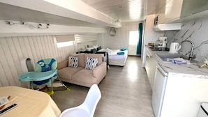 A compact, well-lit room with a kitchenette, a sofa, a dining table, and a high chair.