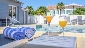 A poolside setting with a lounge chair, a rolled towel, and two drinks on a table.