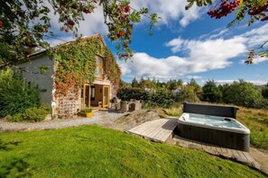 Un edificio de piedra rústico con un porche cubierto y un jacuzzi en un jardín exuberante.