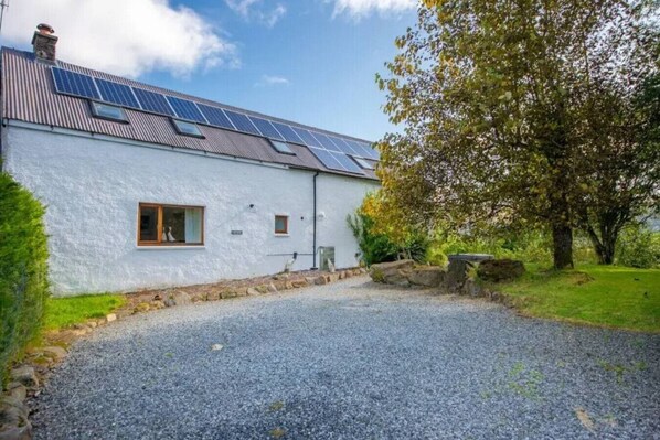 Una casa con paneles solares en el techo, un camino de grava y un árbol a la derecha.