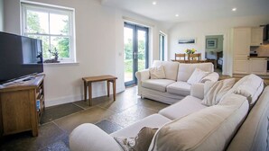 A spacious living room with a large sofa, a television, and a small wooden table. - Wishing Well Cottage at Loch Tay & Hot Tub (Perth and Kinross)