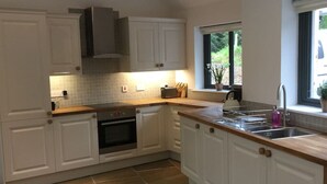 A modern kitchen with white cabinetry, a built-in oven, and a large island with a sink. - Wishing Well Cottage at Loch Tay & Hot Tub (Perth and Kinross)