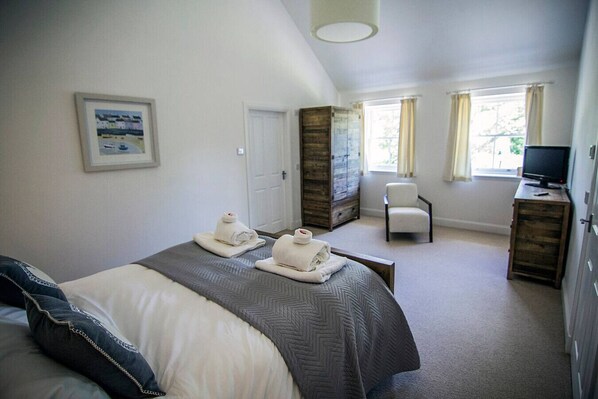 A hotel room with a bed, a chair, a desk with a TV, and a window with curtains.