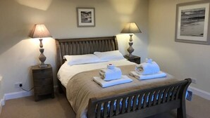 A double bed with a wooden headboard, two bedside tables with lamps, a beige carpet, and two framed pictures on the walls.