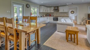 A spacious kitchen with white cabinets, a dining area with wooden furniture, and a living room with a sofa and a TV.