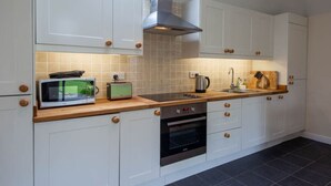 A modern kitchen with white cabinets, a wooden countertop, a built-in oven, a microwave, and a kettle. - Loch Tay Bothy Cottage with Hot Tub (Perth and Kinross)