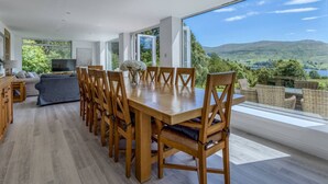 A spacious dining area with a large wooden table and chairs, a sofa, and a television in the background.