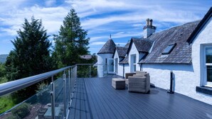 A rooftop deck with a glass balustrade, outdoor seating, and a view of the surrounding landscape.