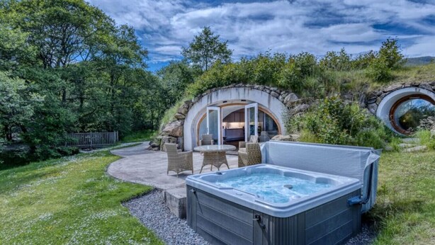 A hot tub with a stone wall backdrop, outdoor seating area, and a view of a natural landscape.